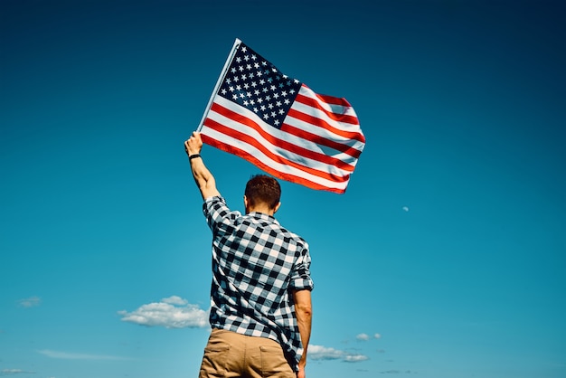 L'homme extérieur de drapeau américain tient le drapeau national des etats-unis contre le ciel bleu nuageux