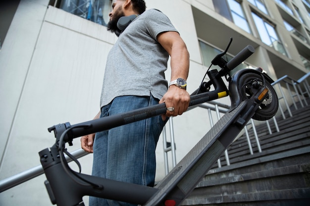 Photo homme à faible angle portant un scooter électrique dans les escaliers