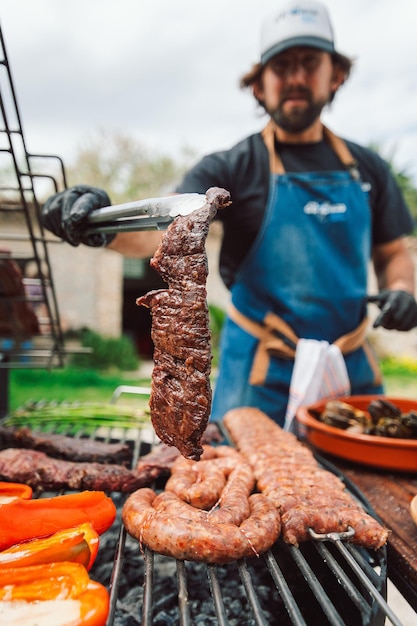 Un homme faisant cuire de la viande sur un gril avec un tablier bleu qui dit 'emba'on it