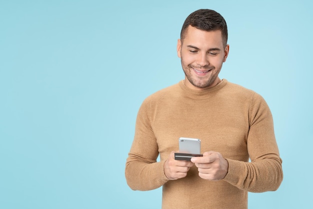 Homme faisant du shopping sur un téléphone intelligent à l'aide d'une carte de crédit isolée sur fond bleu