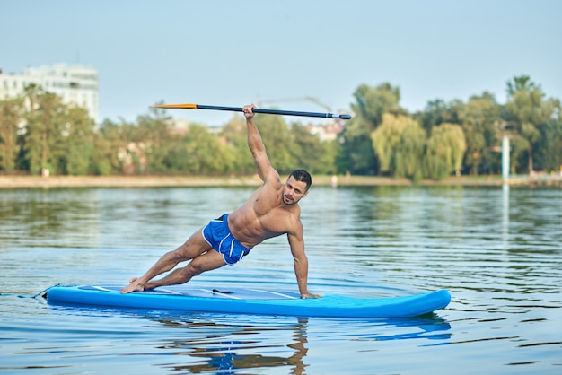 Homme faisant des exercices de planche latérale avec rame à la main sur une planche à pagaie.