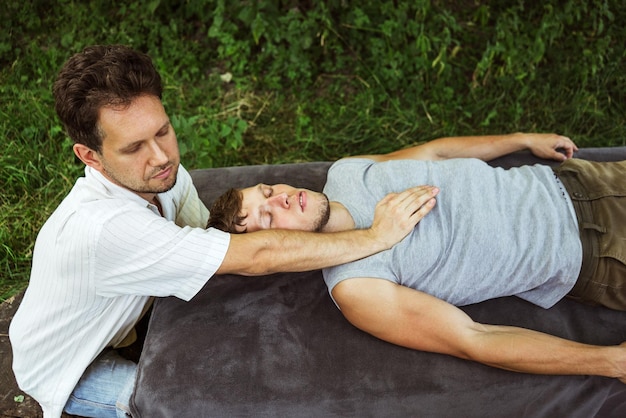 Un homme faisant un massage ostéopathique de la tête et de la poitrine à un gars dans la nature 1