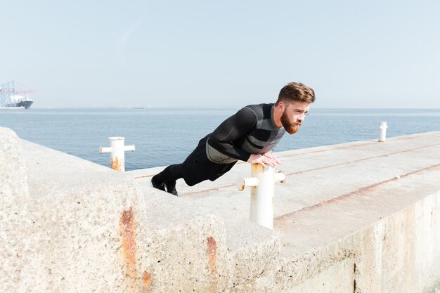 Homme faisant des pompes près de la mer. vue de côté