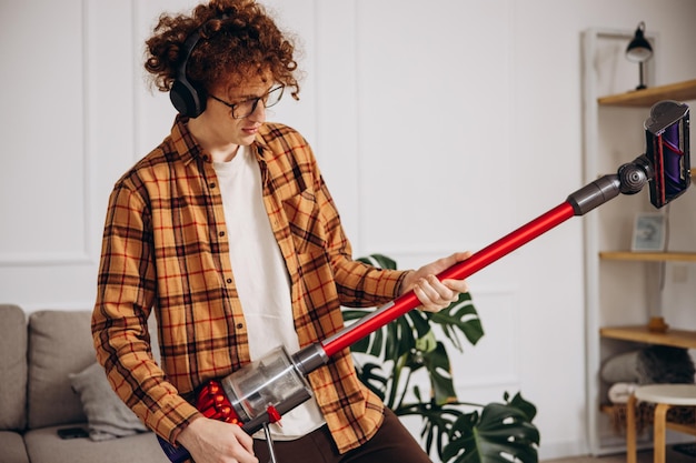 Photo homme faisant des travaux ménagers avec un aspirateur sans fil et écoutant de la musique