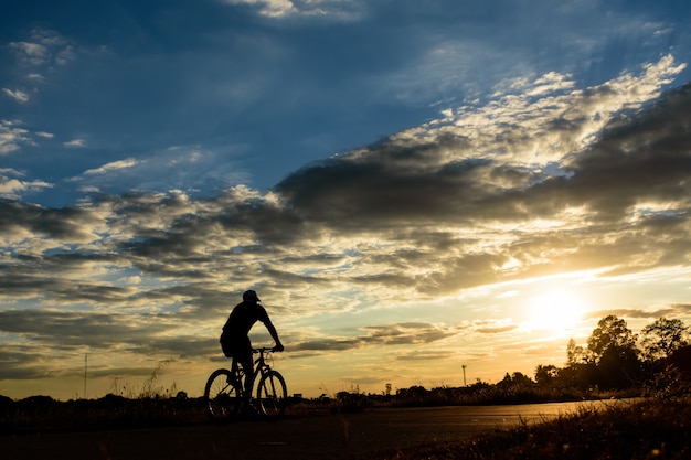 Un homme fait du vélo au coucher du soleil.