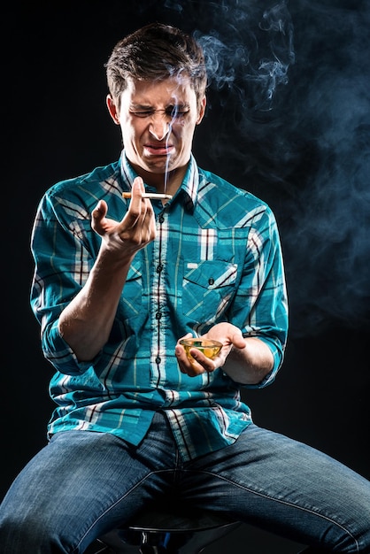 Photo un homme fait une grimace en tenant une cigarette sur un fond noir