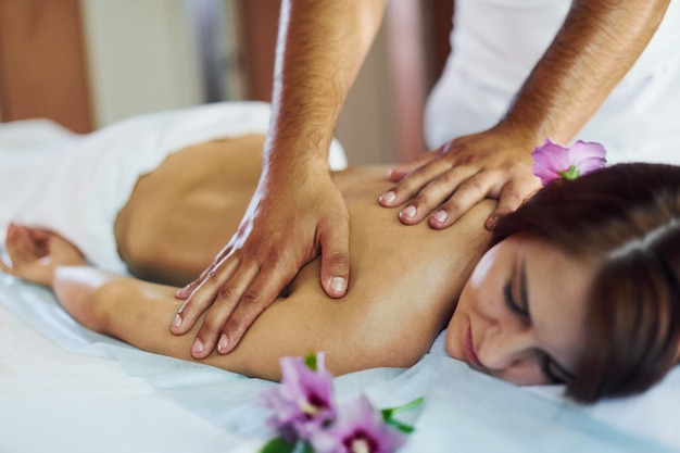 L'homme fait un massage à la jeune femme en serviette blanche à l'intérieur