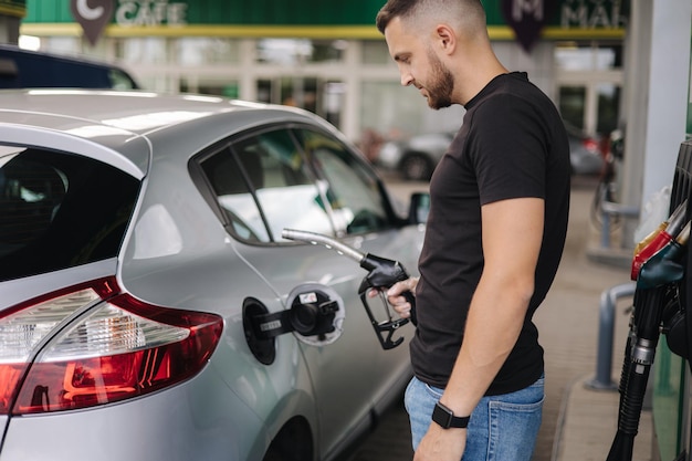 L'homme fait le plein à la station-service mâle remplissant à la main de l'essence benzine dans une voiture à l'aide d'une buse de carburant