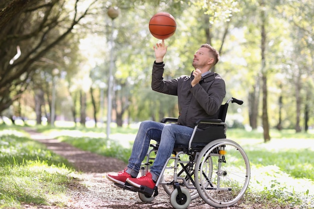 Photo l'homme fait tourner le basket-ball alors qu'il était assis en fauteuil roulant dans la réhabilitation du parc après une blessure à la colonne vertébrale et