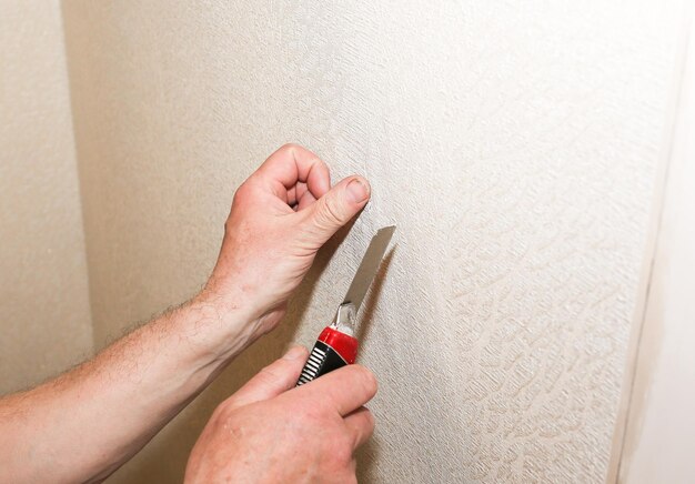 L'homme fait un trou dans le papier peint Installation de la prise Travaux de réparation d'entretien rénovation dans l'appartement Restauration à l'intérieur