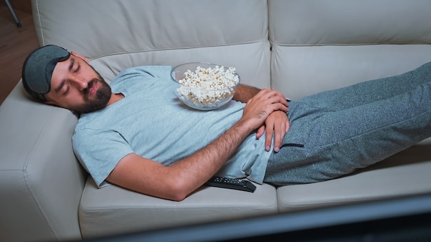 Homme fatigué allongé sur le canapé en regardant un film