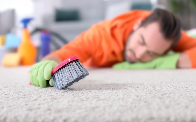 Homme fatigué après avoir nettoyé le tapis dormant sur le sol à la maison