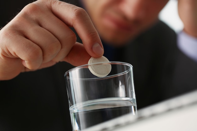 Un homme fatigué a mis une tablette dans du verre avec de l'eau pour arrêter les maux de tête en raison d'une grande charge de travail