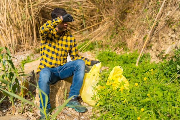 Homme fatigué ramasser des ordures dans une forêt Écologie nettoyer la nature à partir de plastiques
