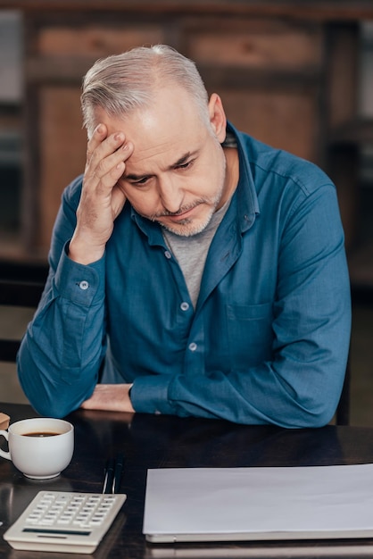 Homme fatigué tenant la tête et regardant la tasse avec du café