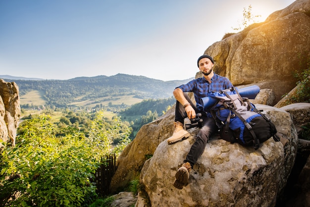 Homme fatigué voyageur assis sur les rochers et tenant un sac à dos