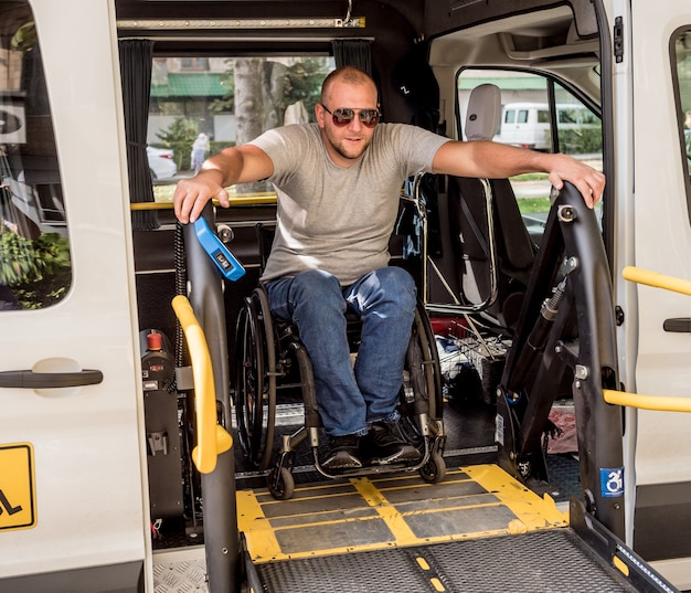 Un homme en fauteuil roulant sur un ascenseur d'un véhicule pour personnes handicapées.