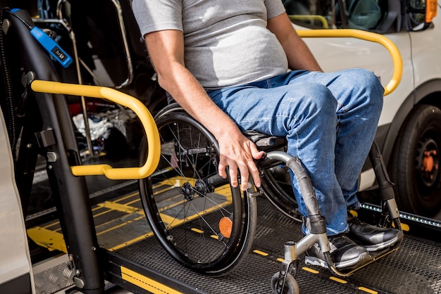 Un homme en fauteuil roulant sur un ascenseur d'un véhicule pour personnes handicapées.