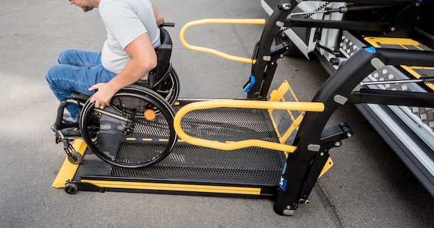 Un homme en fauteuil roulant sur un ascenseur d'un véhicule spécialisé pour les personnes handicapées.