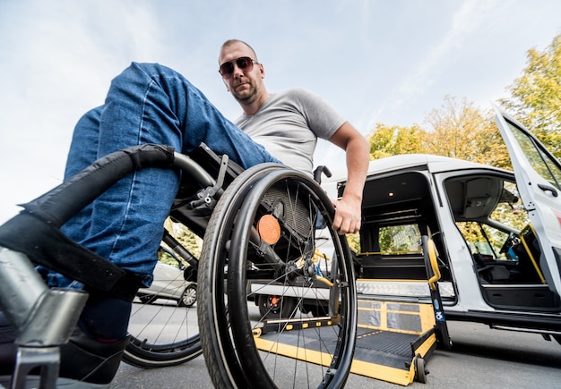 Un homme en fauteuil roulant sur un ascenseur d'un véhicule spécialisé pour les personnes handicapées.