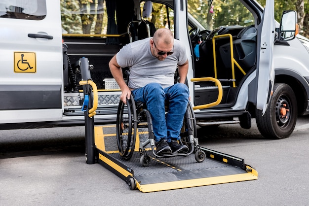 Un homme en fauteuil roulant sur un ascenseur d'un véhicule spécialisé pour les personnes handicapées.