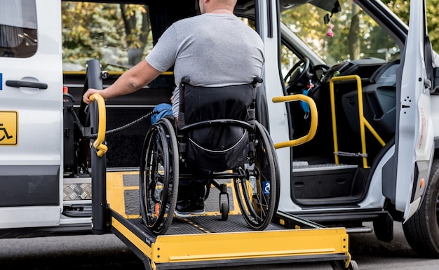 Un homme en fauteuil roulant sur un ascenseur d'un véhicule spécialisé pour les personnes handicapées.