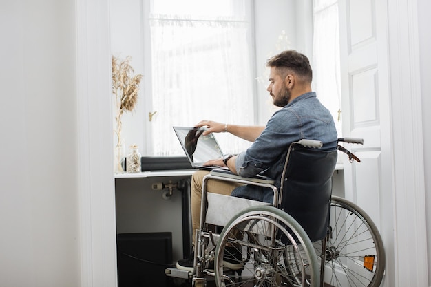 Homme en fauteuil roulant finissant le travail et fermant l'ordinateur portable à la maison