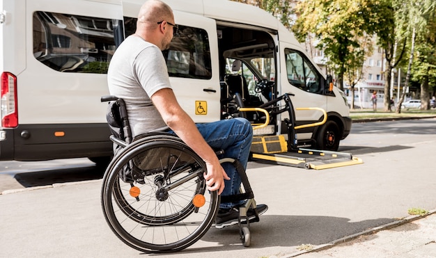 Un homme en fauteuil roulant se déplace vers l'ascenseur d'un véhicule spécialisé pour personnes handicapées.