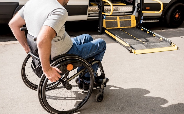 Un homme en fauteuil roulant se déplace vers l'ascenseur d'un véhicule spécialisé pour personnes handicapées.