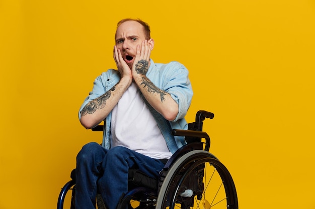 Un homme en fauteuil roulant surpris avec des tatouages sur ses bras est assis sur un fond de studio jaune le concept de santé est une personne handicapée