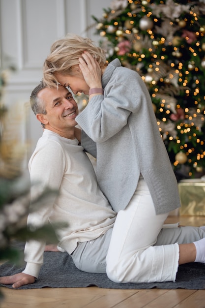 homme et femme adultes s'assoient sur le sol près de l'arbre de noël et s'embrassent