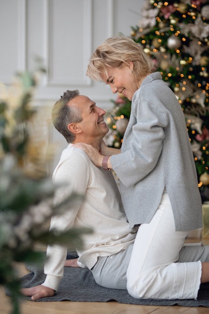 homme et femme adultes s'assoient sur le sol près de l'arbre de noël et s'embrassent