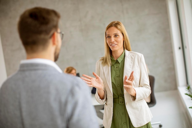 Un homme et une femme d'affaires discutent à l'intérieur du bureau avec des jeunes gens qui travaillent derrière eux.