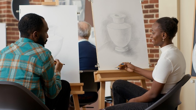 Homme Et Femme Afro-américains Dessinant La Conception D'objets Avec Des Outils Artistiques Dans Le Cadre D'un Programme D'ateliers éducatifs. Apprendre à Dessiner Des Illustrations Sur Toile Avec Un Chevalet Pour Les Résolutions Du Nouvel An.