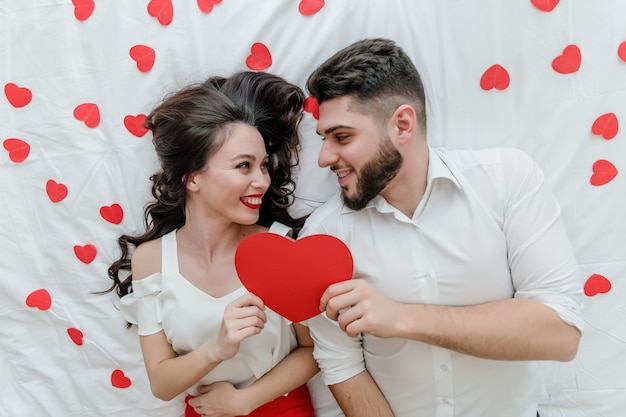 Homme et femme amoureux sur lit avec carte de Saint Valentin en forme de coeur rouge à la maison
