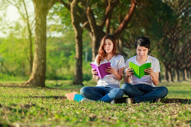 homme et femme assis et lisant un livre dans le parc