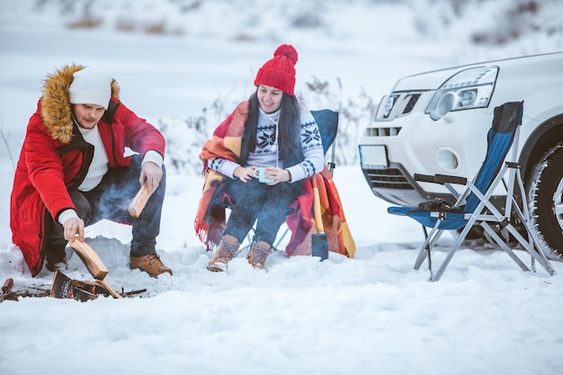 Homme avec une femme assise sur des chaises près d'un feu de camp en hiver Voyage en voiture