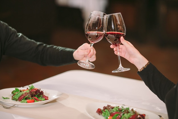 Homme et femme buvant du vin rouge. Sur la photo, gros plan des mains avec des lunettes.