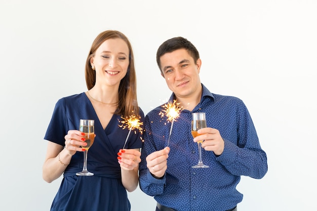 Homme et femme célébrant la fête de Noël ou du nouvel an avec des feux de Bengale et des verres de champagne sur fond blanc.