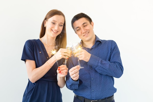 Homme et femme célébrant la fête de Noël ou du nouvel an avec des feux de Bengale et des verres de champagne sur fond blanc.