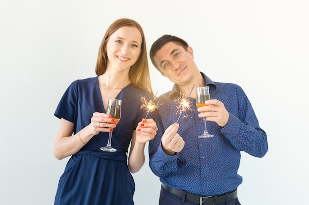 Homme et femme célébrant la fête de Noël ou du nouvel an avec des feux de Bengale et des verres de champagne sur fond blanc.