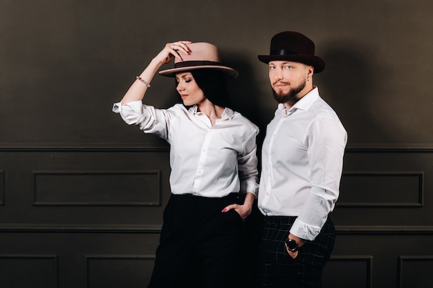 Un homme et une femme en chemises blanches et chapeaux sur fond noir. Un couple amoureux pose à l'intérieur du studio.