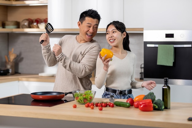Homme et femme coréens positifs cuisinant ensemble à la maison