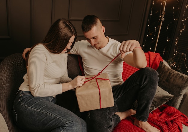 Homme et femme couple amoureux ouvrir les coffrets cadeaux délier un arc près de l'arbre de Noël