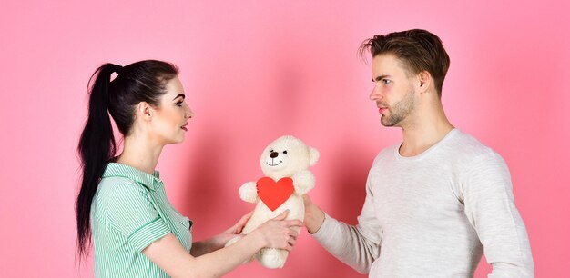 L'homme et la femme couple amoureux tiennent des cartes de Saint Valentin coeur et ours en peluche sur fond rose. Couple romantique amoureux. Saint Valentin et amour. Concept de cadeau mignon. Bel homme et jolie fille amoureuse.