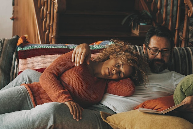 Homme et femme couple à la maison profiter du temps et se détendre ensemble allongé sur le canapé Mari lisant un livre et femme dormant sur lui dimanche activité de loisirs concept d'intérieur style de vie Amour et romance