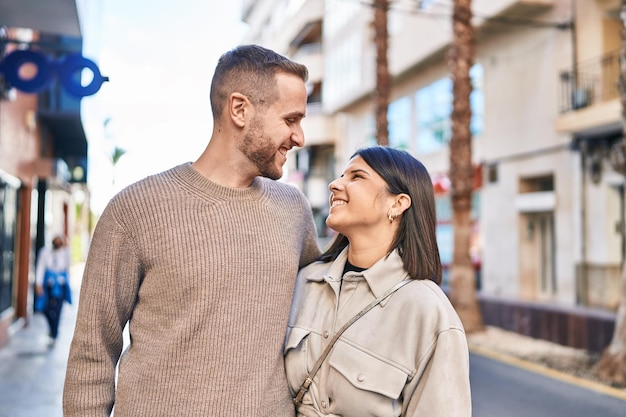 Homme et femme couple souriant confiant s'étreignant debout dans la rue