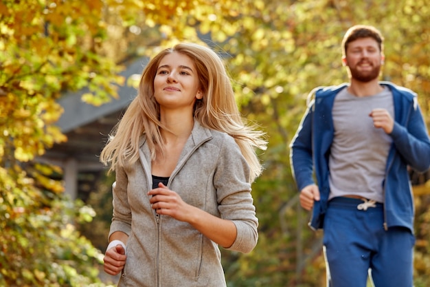 Homme et femme courent ensemble dans la forêt d'automne, homme et femme sportive athlétique en tenue de sport