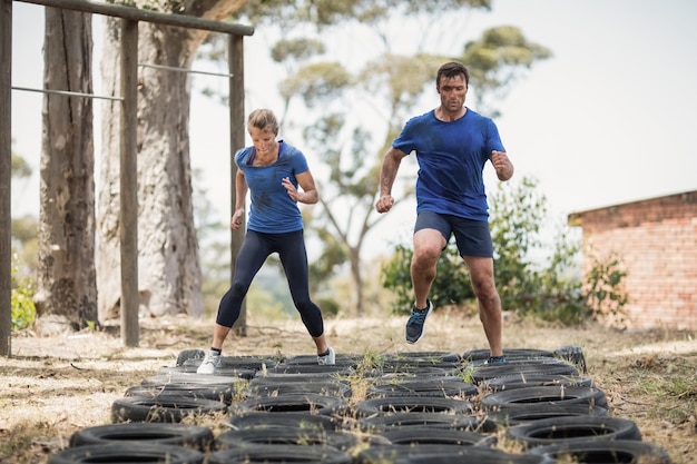 Homme et femme en cours d'exécution sur le pneu pendant la course d'obstacles dans le camp d'entraînement