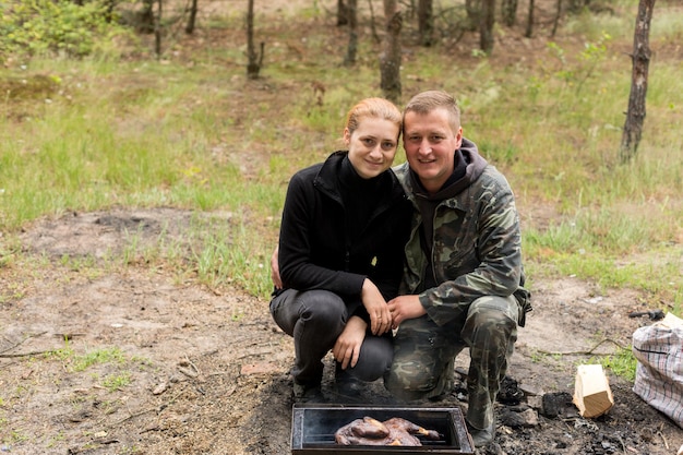 Un homme et une femme cuisinent sur un feu de camp dans les bois.